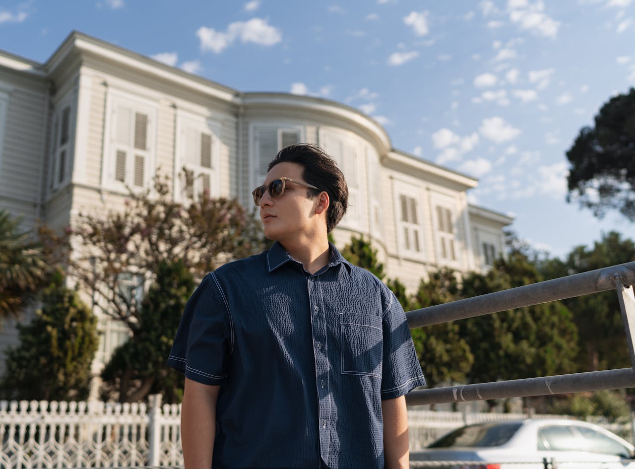 Stylish man in sunglasses outdoors, showcasing modern summer fashion against elegant architecture.