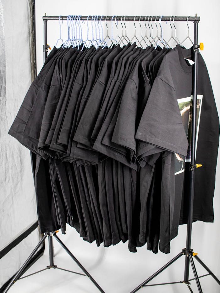 Collection of plain black t-shirts neatly hung on a metal rack in a professional studio setting.